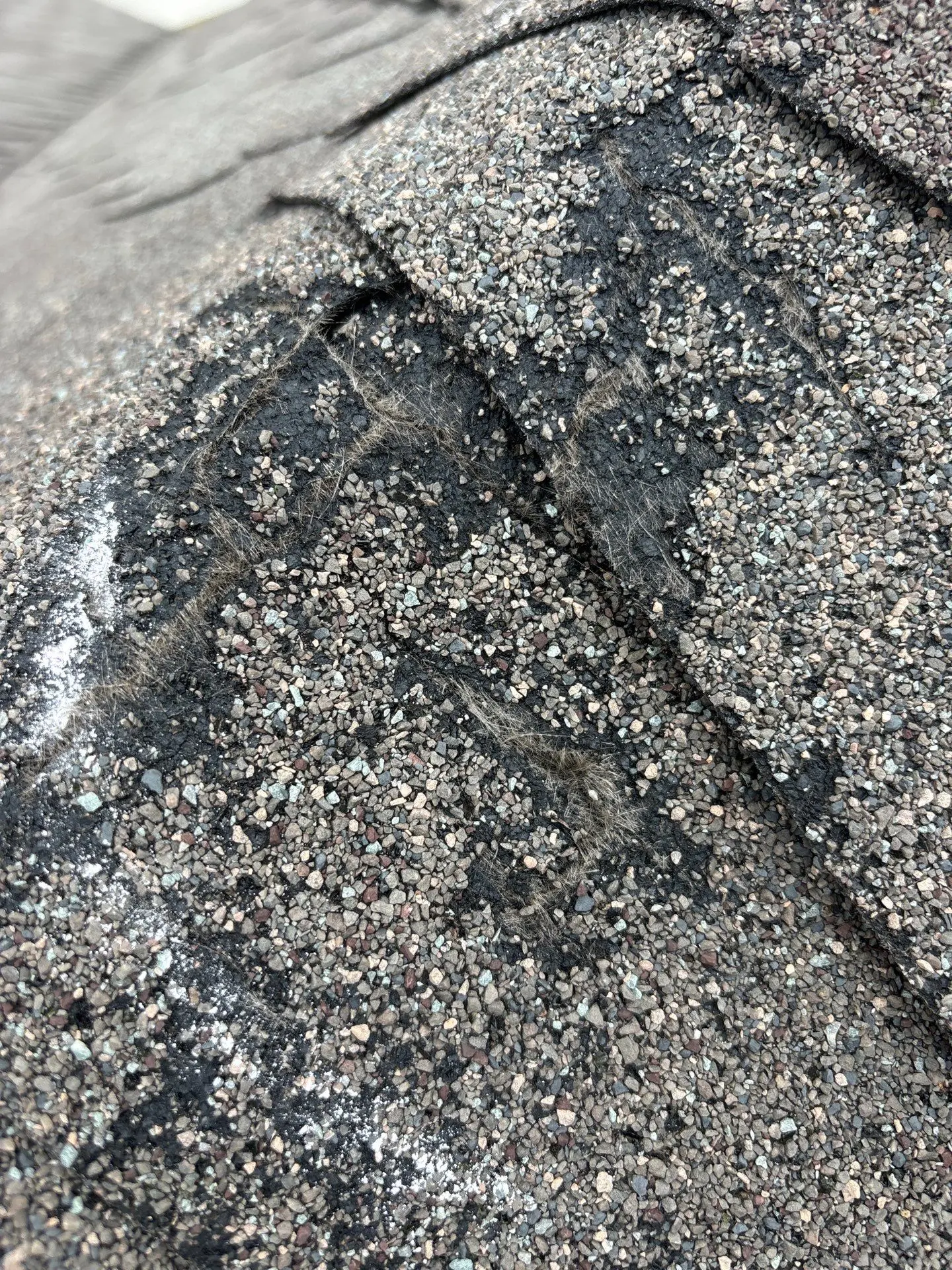 Close view of a torn shingle surface with exposed fibers